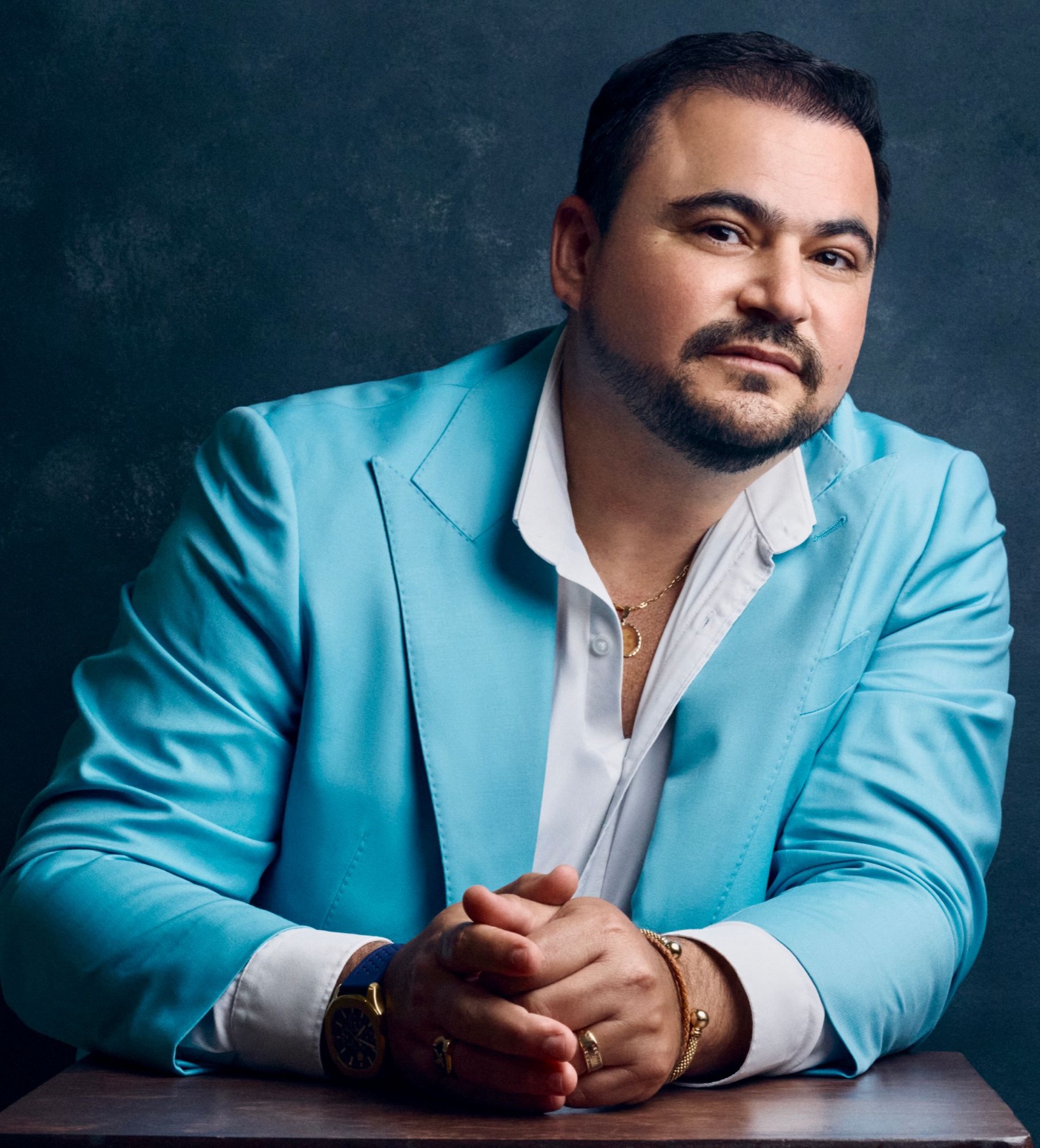 El Dr. Hendry Pascual con saco turquesa y camisa blanca, sobre un fondo azul oscuro
